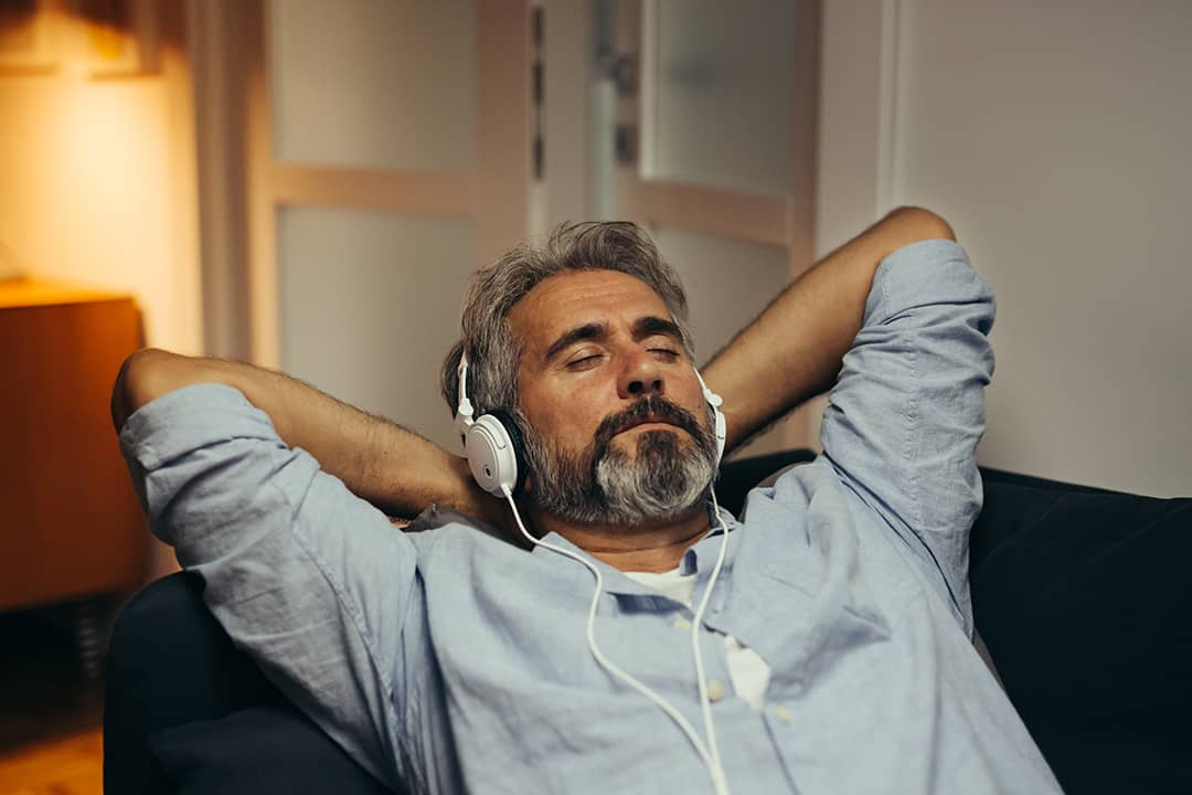 A relaxed middle age man listening to music on the sofa.